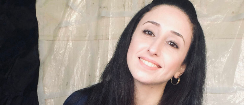 Picture of Nayrouz Qarmout. Smiling with dark long hair and in a black top, her head tilted to oneside.